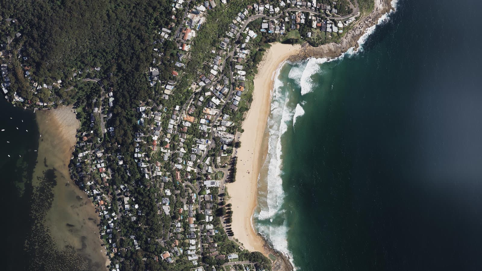 Aerial view of Whale Beach's rust-orange crescent between two green headlands, with Pittwater beyond