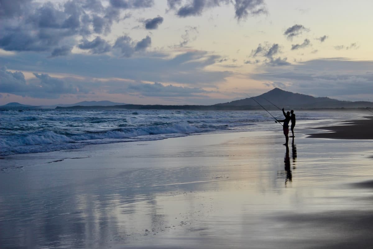 Two fishers silhouetted on the wet sand of Stockton Beach in low light, the beach otherwise empty